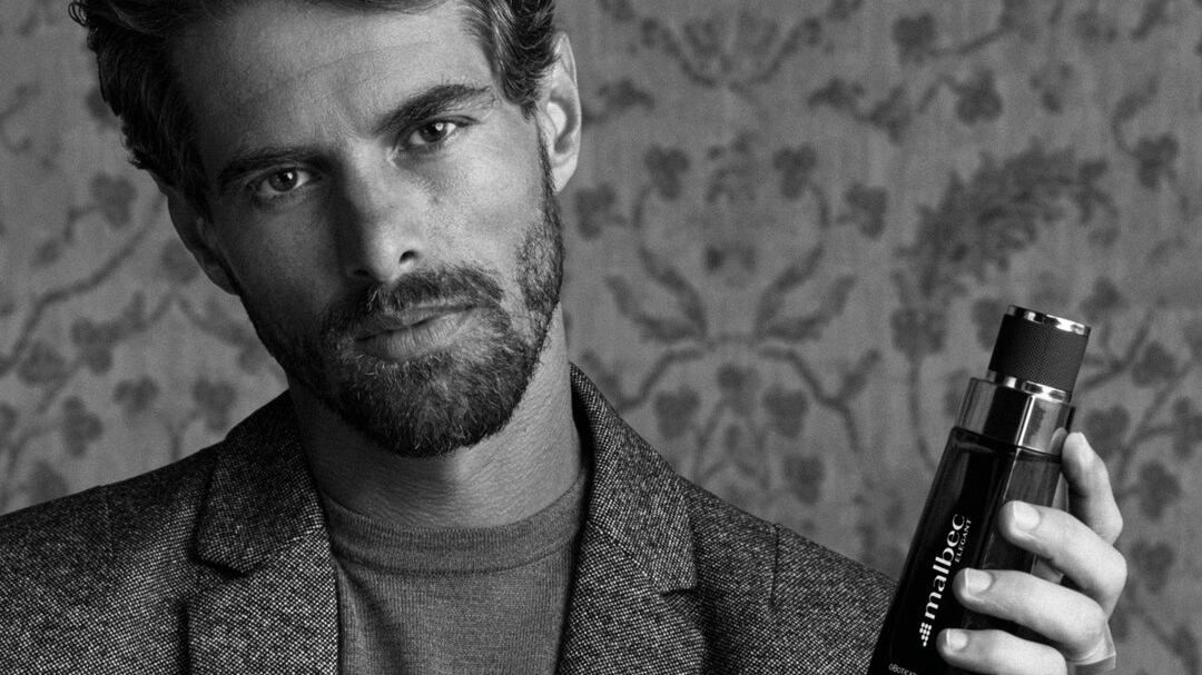 Imagem em preto e branco de homem de terno segurando frasco de perfume Malbec Elegant