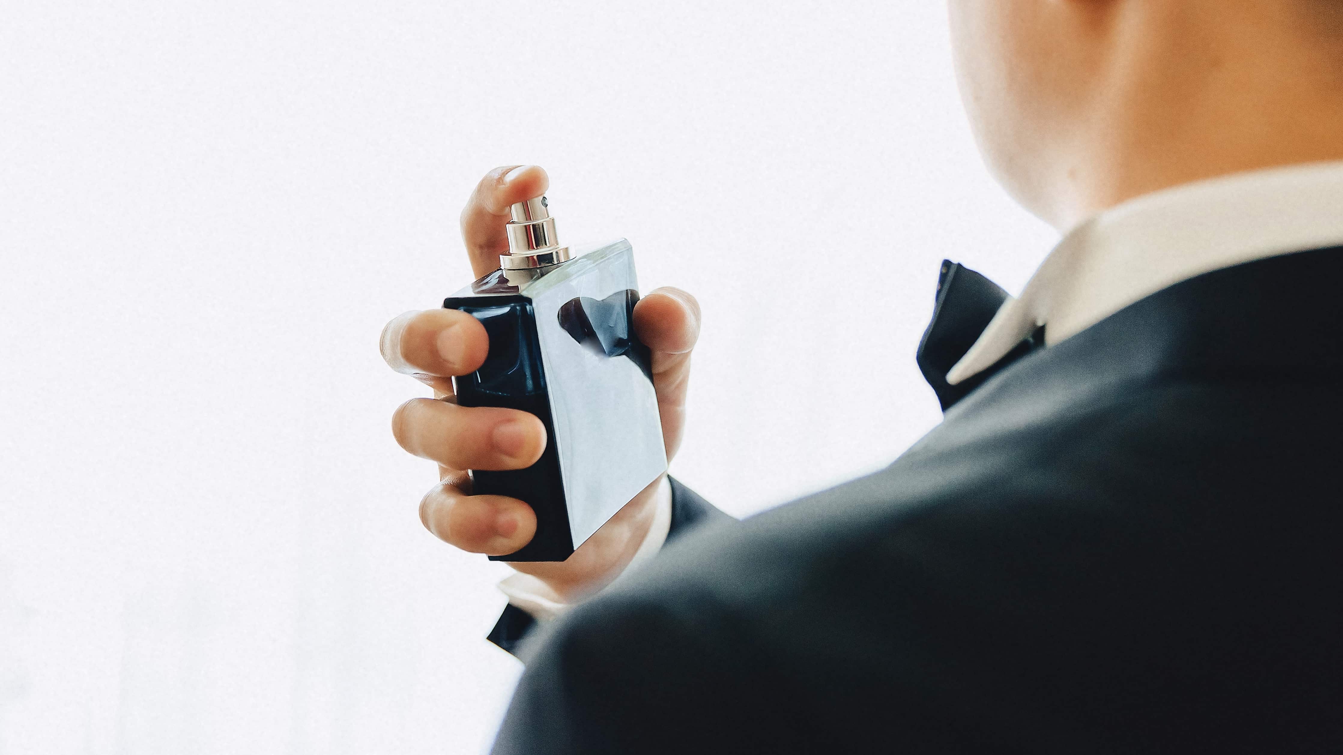 Imagem: homem de terno espirrando frasco de perfume azul