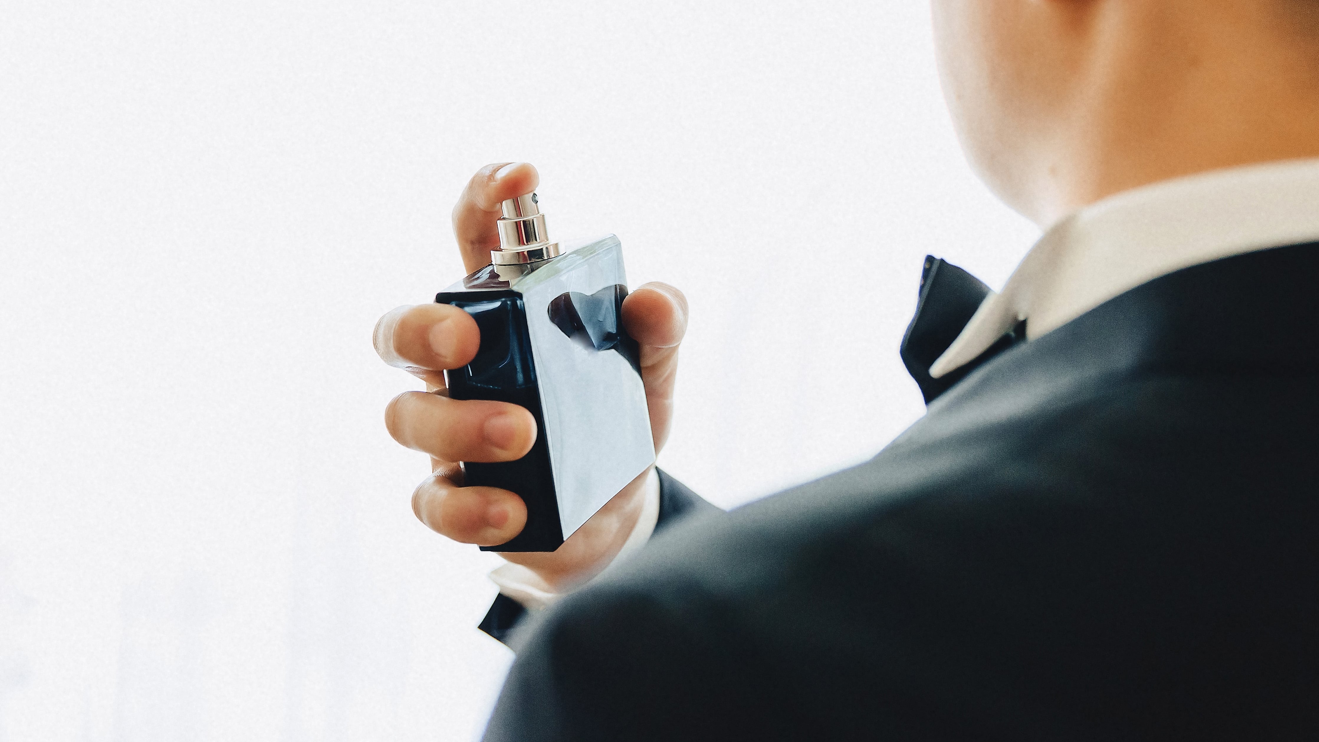 Imagem: homem de terno espirrando frasco de perfume azul